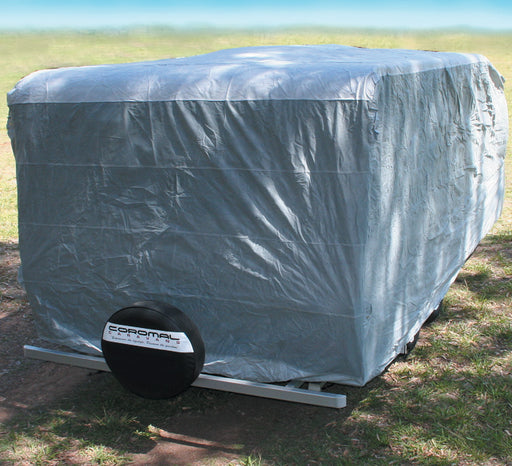 A Prestige Pop Top Caravan, adorned with a UV-stabilized triple-layer cover in gray, stands on the grass. At the rear, a spare tire is mounted with "Coronal" prominently printed on it. The setup is framed beautifully against a clear blue sky.