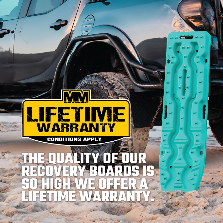 A black off-road vehicle is parked on a sandy beach. Next to it stands an Exitrax Recovery Board Ultimate 1150 in Blood Orange. Text overlay reads: "The quality of our recovery boards is so high we offer a lifetime warranty." A logo with "MM Lifetime Warranty" and "Conditions Apply" is also visible, showcasing unparalleled traction enhancement.