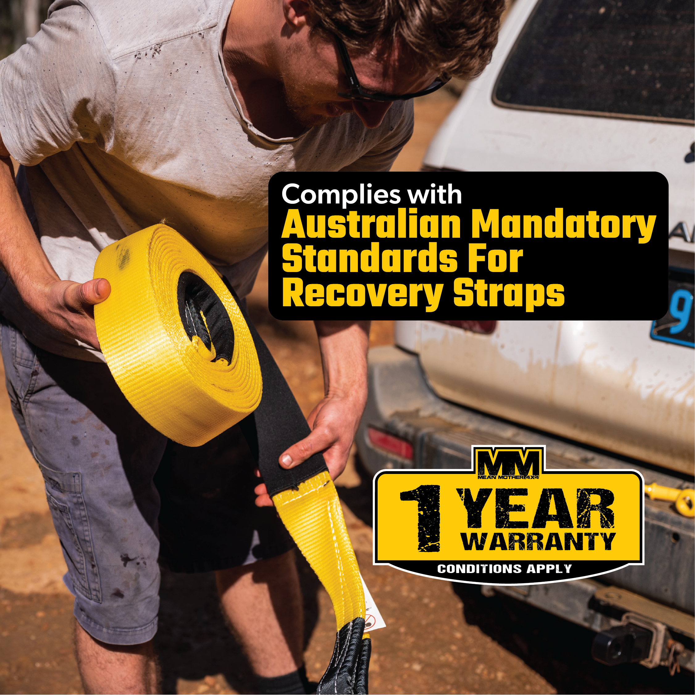 A person unrolls the bright yellow Mean Mother Snatch Strap 8,000kg, expertly crafted with durable nylon webbing, near a vehicle under the sunny sky. The image includes text that underscores compliance with Australian standards for recovery straps and emphasizes a 1-year warranty offer.