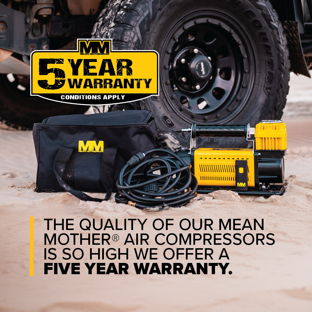 The Air Compressor with Wireless Remote Control 180lpm and its accessories are placed on the sand near a black vehicle tire. The text reads: "Our Mean Mother® air compressors offer unrivaled quality with a powerful Free Air Delivery of 180L/Min, backed by a five-year warranty." A 5-year warranty label is displayed in the upper left corner.