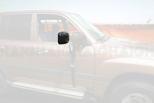 A Mean Mother 4x4 Mirror Head To Suits Mh3015 is mounted on a brown SUV parked on a dirt road, with a large rectangular black mirror visible and a blurred rural landscape of trees and open land in the background.