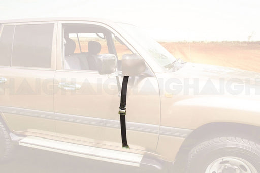 A beige SUV on a dirt road features the Mean Mother 4x4 Mirror Wide Door Base Strap Suits Mh3015 in black, securing the side mirror to the door, with a blurred landscape in the background.