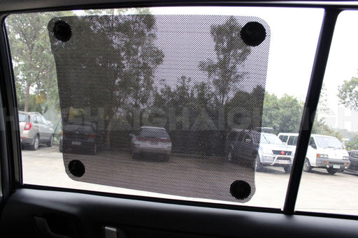 The Mean Mother 4x4 Press'O'Curtain Twin Pack sunshade attaches inside your car window with suction cups, while a parking lot and trees can be seen outside through its tinted mesh material.