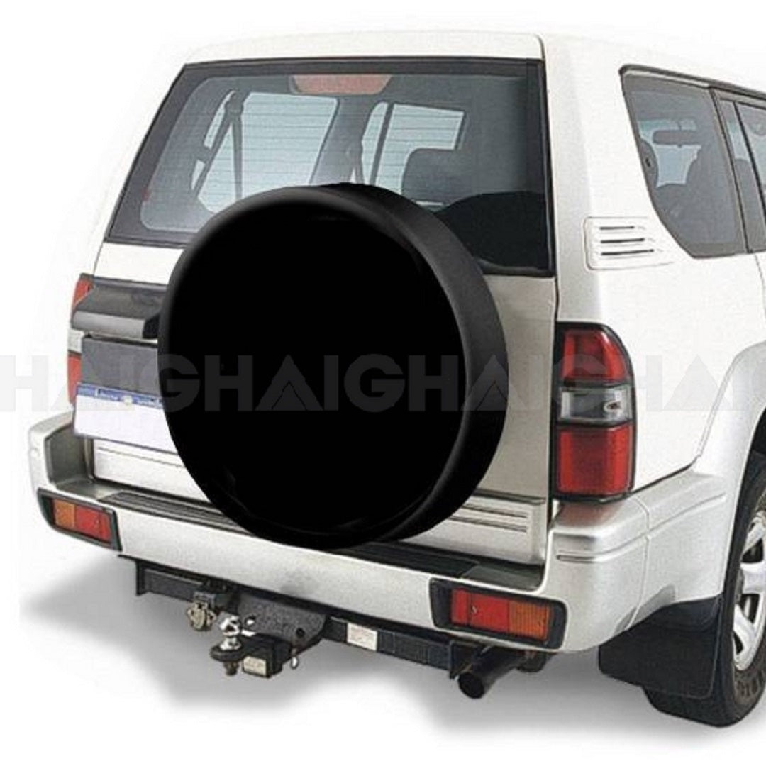 A white SUV is depicted from the rear, highlighting the Cargo Mate 4WD Spare Wheel Cover - 29" made of durable vinyl material mounted on the back door for spare wheel protection. Additionally, the vehicle includes a towing hitch at the bottom, with part of the rear window visible above the wheel cover.