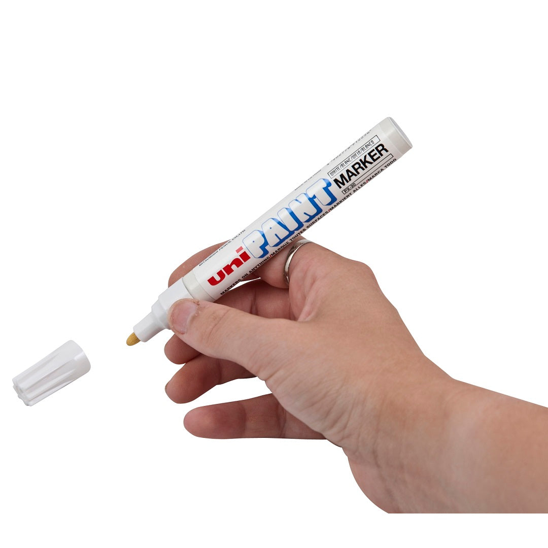 A hand holding a white Drive Tyre Paint Stick with the cap removed. The marker, known for its precise application on materials like raised tire lettering, has a white body with "Drive Tyre Paint Stick" written in blue and red text. The removed cap is placed on the left side of the image against a white background.