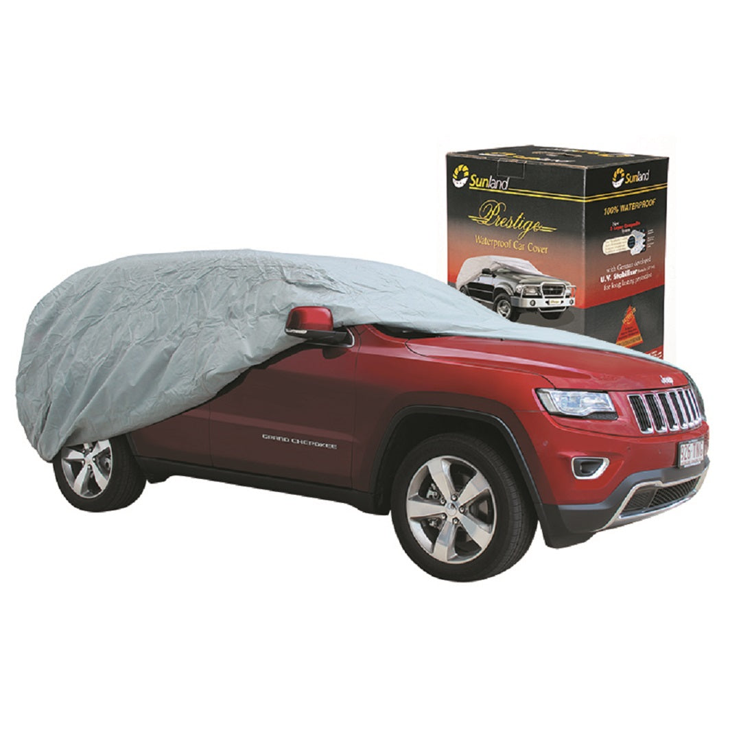 A red SUV, partially draped with a Prestige Premium Waterproof Cover in gray, constructed from 5-layer breathable fabric, stands next to its corresponding product box. The packaging highlights the extra large cover for 4WDs/SUVs and dual cab utes with canopies up to 5.56 meters, emphasizing its UV-stabilized protection.