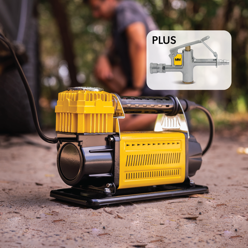 A Mean Mother Adventurer 4 â€“ 180lpm Air Compressor Bundle, in yellow and black, sits on a gravel surface, connected to a tire in the background. An inset image shows a close-up of a tire inflator attachment labeled "PLUS". A person is crouched in the background, slightly blurred.