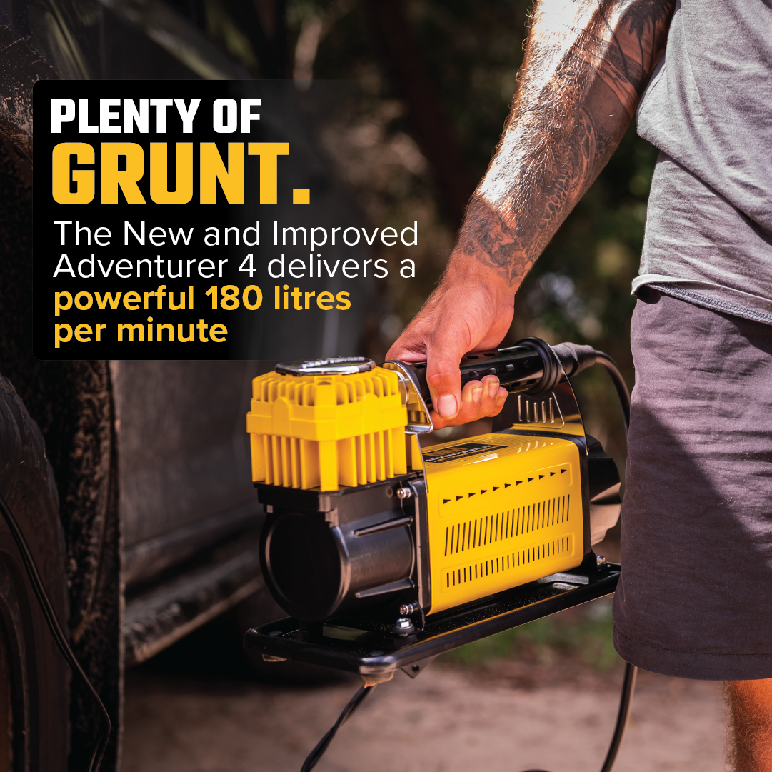 Close-up of a person holding a yellow air compressor labeled "Mean Mother Adventurer 4 â€“ 180lpm Air Compressor Bundle" near a vehicle. The text reads, "PLENTY OF GRUNT. The New and Improved Mean Mother Adventurer 4 delivers a powerful 180 litres per minute." The person, sporting a tattoo on their forearm and gray shorts, is ready with this top-notch 4x4 Air Compressor from Mean Mother.