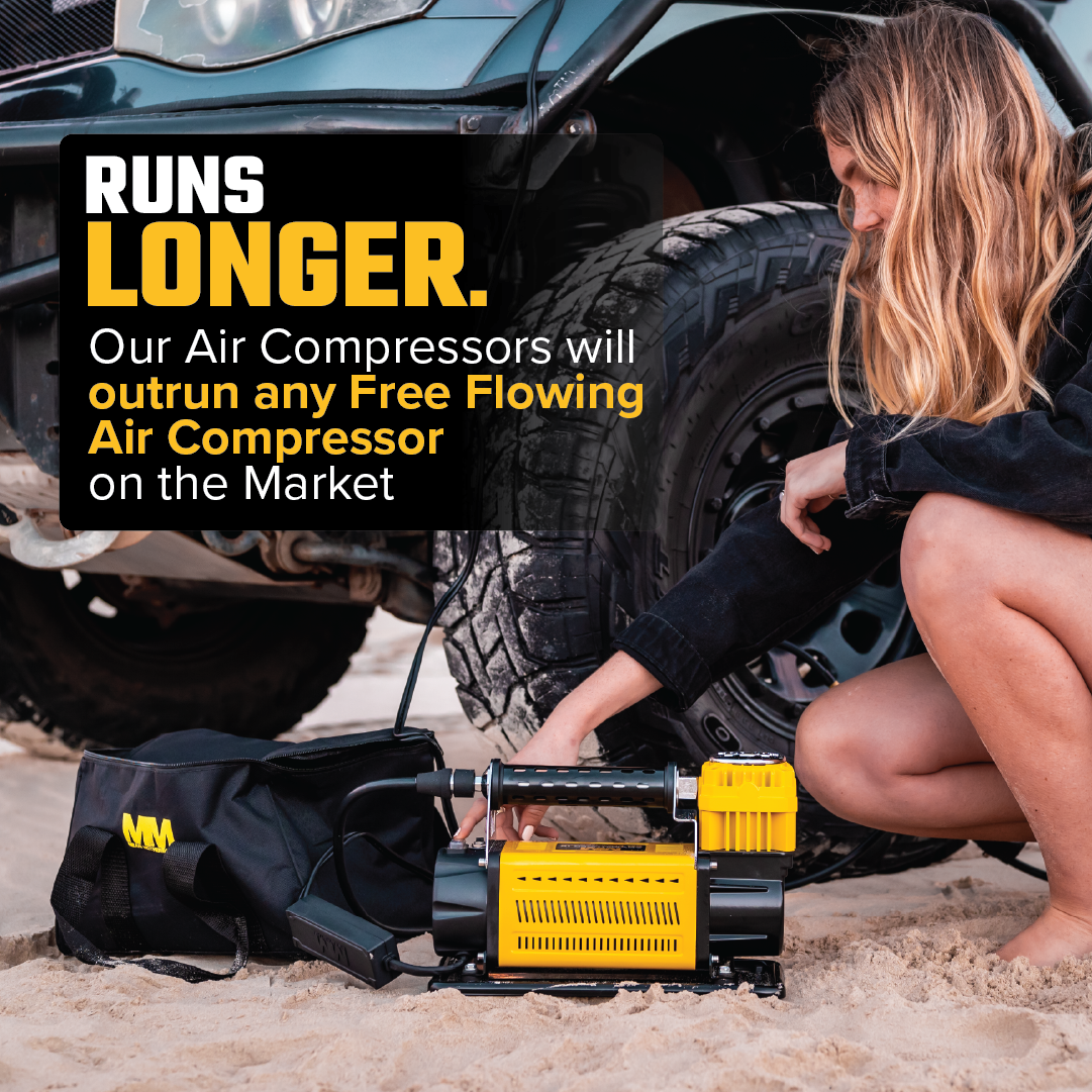 A person with long hair is kneeling next to a car tire on a sandy surface, using a Mean Mother Adventurer 4 â€“ 180lpm Air Compressor Bundle. The text on the image reads: "RUNS LONGER. Our Air Compressors will outrun any Free Flowing Air Compressor on the Market." The air compressor and a carrying bag are visible.